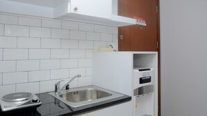 A kitchen with white tiled backsplash, a stainless steel sink, a black countertop, and a built-in oven. - Unique And Fresh 1Br Signature Park Grande Apartment (Jakarta)