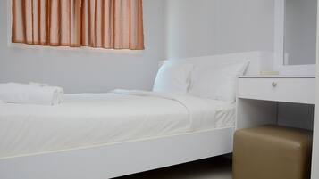 A neatly made bed with white linens, a brown ottoman, a white dresser, and a mirror above it.
