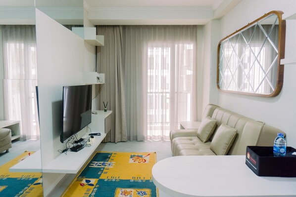 A modern living room with a flat-screen TV, a beige sofa, a coffee table, and a patterned rug. - Great Choice And Comfort 2Br At Signature Park Grande Apartment (Jakarta)