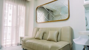 Un salon moderne avec un canapé beige, un grand miroir et une petite table d’appoint blanche.