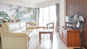 A living room with a sofa, a coffee table, a TV, and a fan. - Elegant And Homey 2Br Apartment At Puri Casablanca (Jakarta)