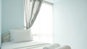 A neatly made bed with white linens and pillows, a window with sheer curtains, and a pair of rolled towels on the bed. - Elegant And Homey 2Br Apartment At Puri Casablanca (Jakarta)