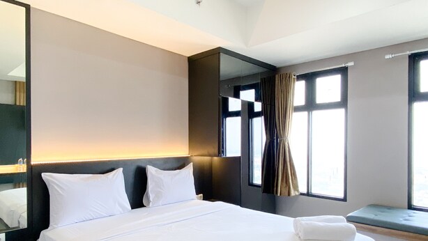 Una habitación de hotel con una cama grande, una mesita de noche, un espejo y una ventana con cortinas.
