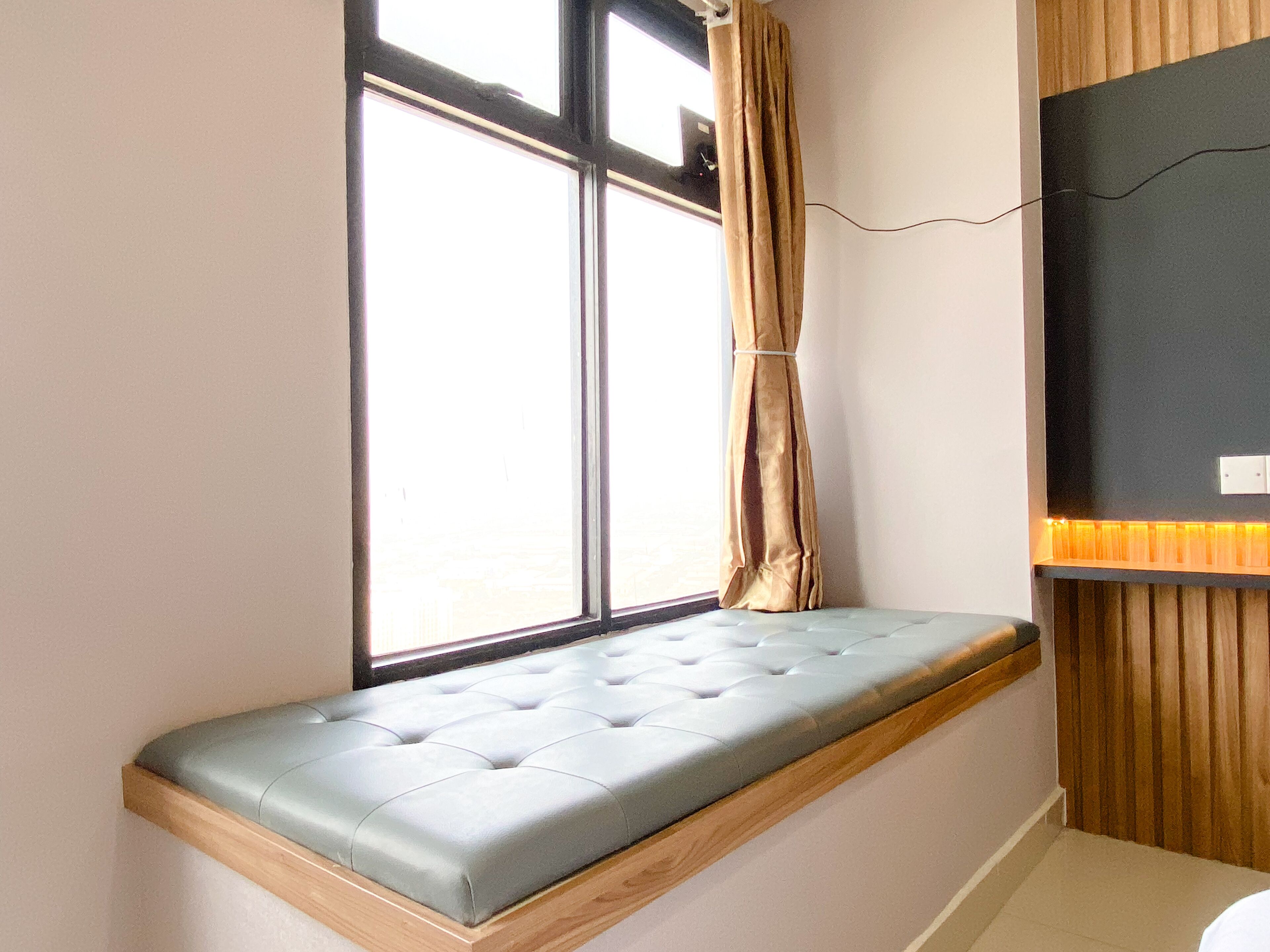 Een hoekappartement met een ingebouwde bank, een raam met gordijnen en een aan de muur bevestigde televisie.