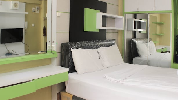 A hotel room with a bed, a desk, a mirror, and a wardrobe. - Nice And Comfortable Studio At Bassura City Apartment Near Mall (Jakarta)