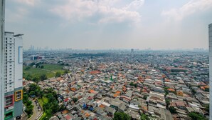 A high-rise building overlooking a densely packed urban area with numerous buildings and a clear sky. - Nice And Comfortable Studio At Bassura City Apartment Near Mall (Jakarta)