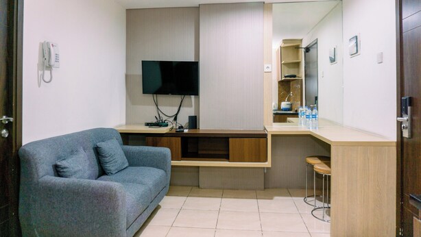 A modern hotel room with a grey sofa, a TV, a wooden counter, and a mirror. - Cozy Stay 2Br Annora Living Apartment (Tangerang)