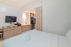 A hotel room with a bed, a desk with a flat-screen TV, a small kitchenette, and a wardrobe. - Best Deal And Comfy Tamansari Sudirman Studio Apartment (Jakarta)