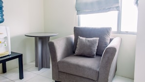 Una habitación pequeña y moderna con un sillón gris, una mesita redonda y una cafetera.