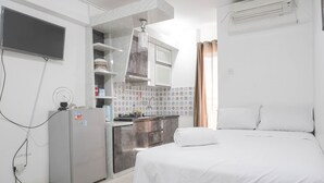 Ett kompakt hotellrum med en säng, ett litet pentry, ett litet kylskåp och en luftkonditioneringsanläggning.