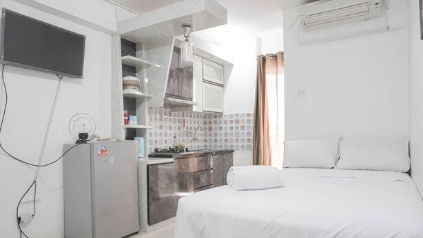 Una habitación de hotel compacta con una cama, kitchenette, un refrigerador pequeño y aire acondicionado.