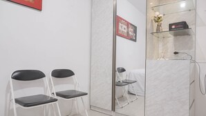 Una habitación con dos sillas plegables, un aparador de vidrio con una bolsa de viaje, y un espejo que refleja la habitación.