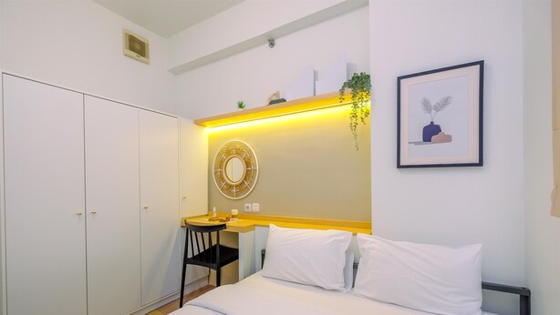 A bedroom with a bed, bedside table, chair, wardrobe, and a wall-mounted mirror.