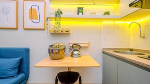 A compact kitchen with a wooden table, a black chair, a blue sofa, and a sink.