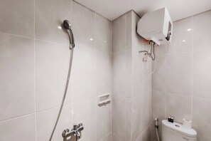 Bathroom features a shower with handheld showerhead and wall-mounted control, alongside a toilet with water heater and paper towel dispenser.
