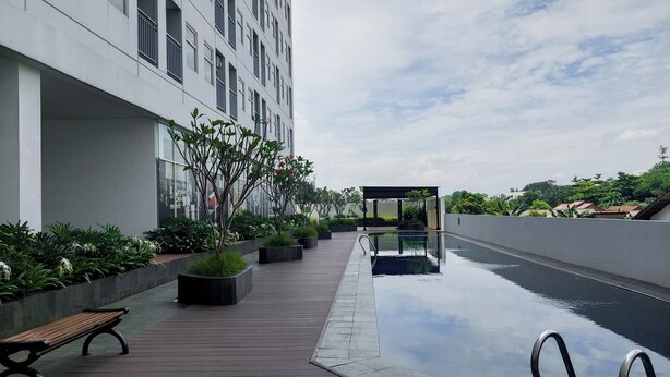A modern building with a rooftop pool, wooden deck, and potted plants. - Homey And Comfortable Studio At Serpong Garden Apartment (Cisauk)