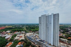 A high-rise building with a modern design, surrounded by a mix of residential and commercial buildings, and a green landscape in the background.