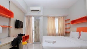 Une chambre d’hôtel avec un lit, un bureau et une chaise, une télévision et des étagères orange.