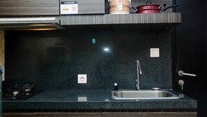 A modern kitchen with a black countertop, stainless steel sink, and a gas stove. - Cozy And Elegant 1Br At The Wave Apartment Kuningan (Jakarta)