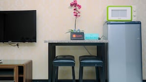 A kitchenette with a flat-screen TV, a microwave, a refrigerator, and two bar stools. - Cozy And Elegant 1Br At The Wave Apartment Kuningan (Jakarta)