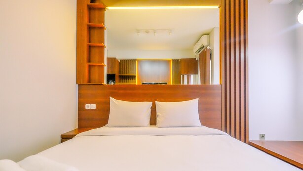 Un lit bien fait, avec du linge de lit blanc et des oreillers, une tête de lit en bois et un grand miroir qui reflète une salle de bain moderne.