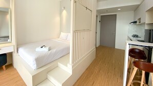 A bedroom with a bed, a desk, and a chair. There is a staircase leading to another room. - Homey And Elegant Studio Vasanta Innopark Apartment (Cikarang)