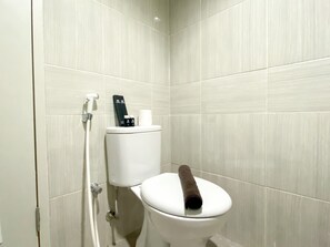 A modern bathroom with a white toilet, a towel on the seat, and a hand dryer on the wall. - Homey And Elegant Studio Vasanta Innopark Apartment (Cikarang)