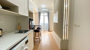 A modern kitchen with a washing machine, a dining area with two chairs, and a view through a glass door. - Homey And Elegant Studio Vasanta Innopark Apartment (Cikarang)