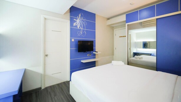 A hotel room with a bed, a TV mounted on the wall, a mirror, and a door. - Strategic And Comfy 2Br Apartment At Trillium Residence (Surabaya)