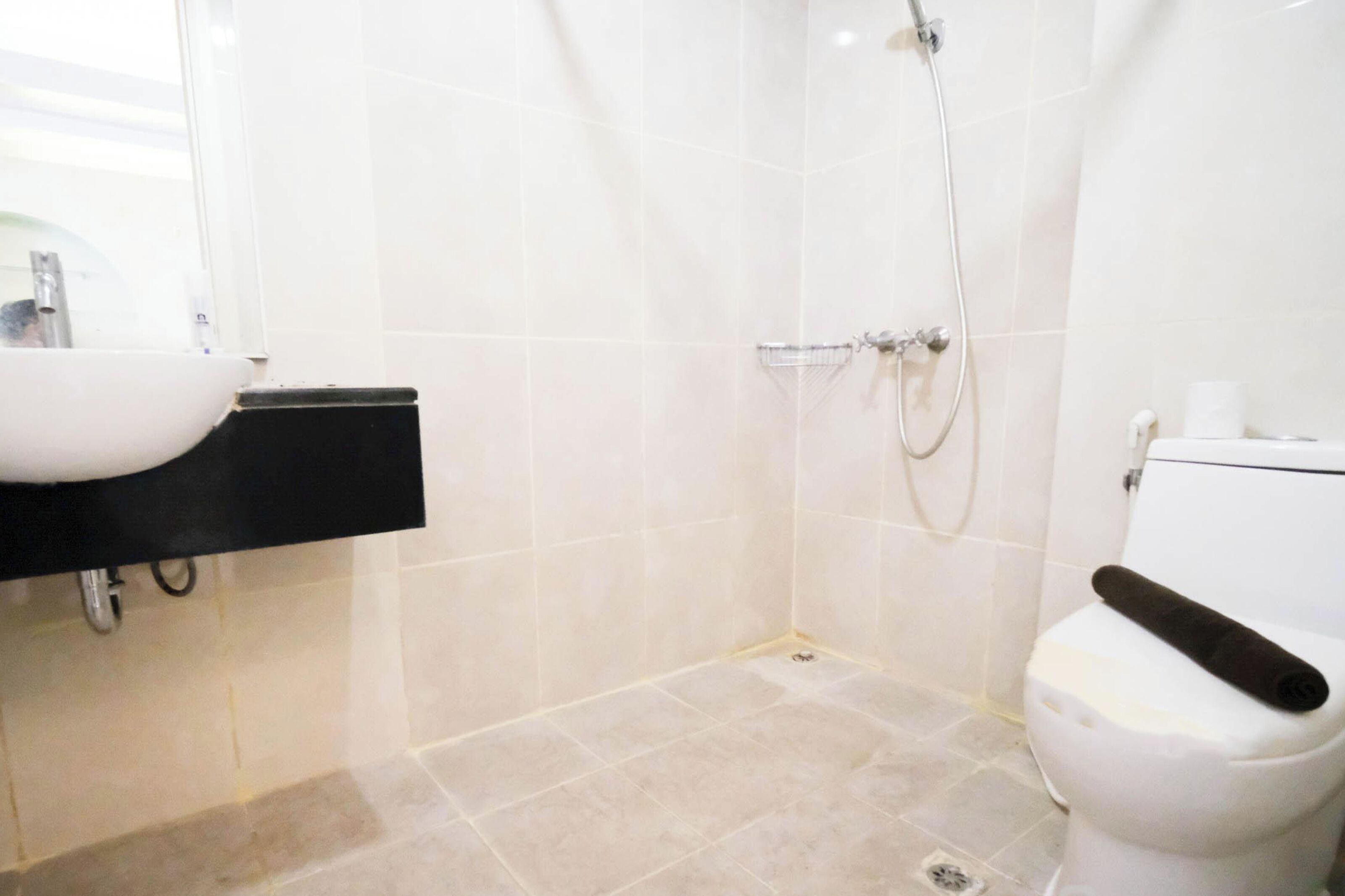 A bathroom with a white sink, a black countertop, a white toilet, and a shower area with beige tiles.