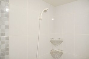 A bathroom with white tiles, a showerhead, and a clear glass shelf.