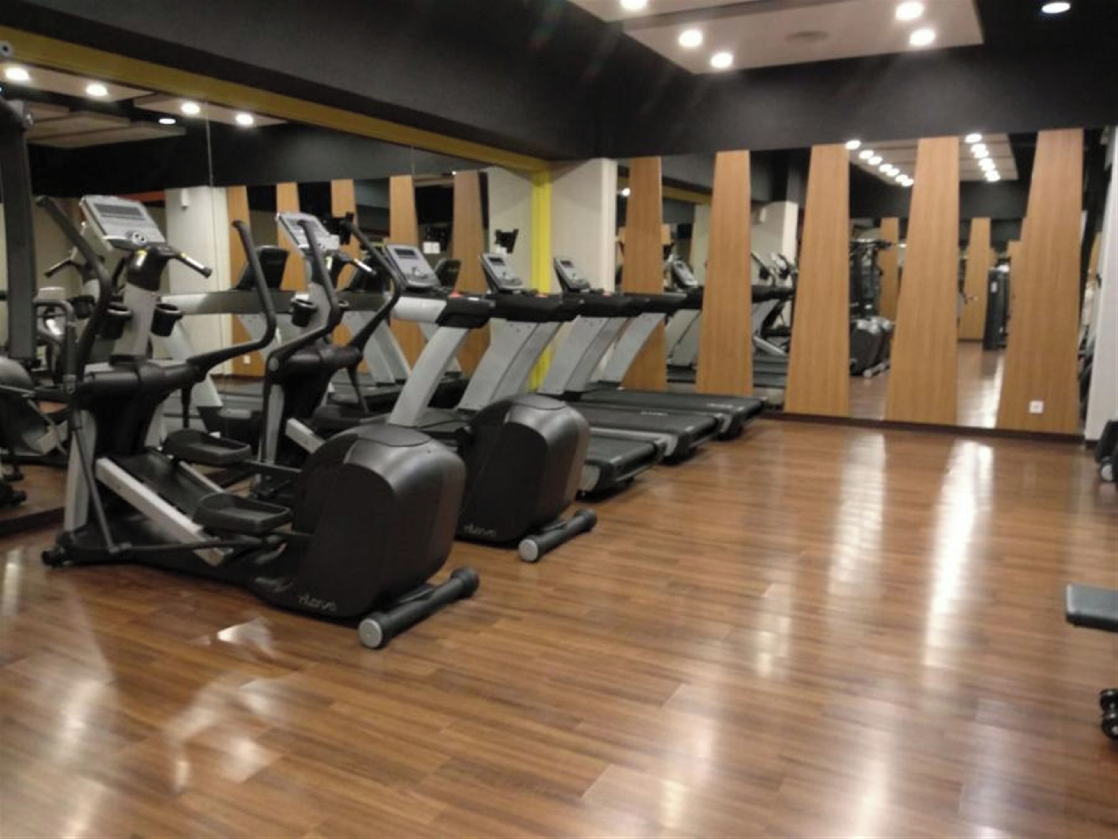 A gym with multiple treadmills and exercise equipment, wooden flooring, and mirrors on the walls.
