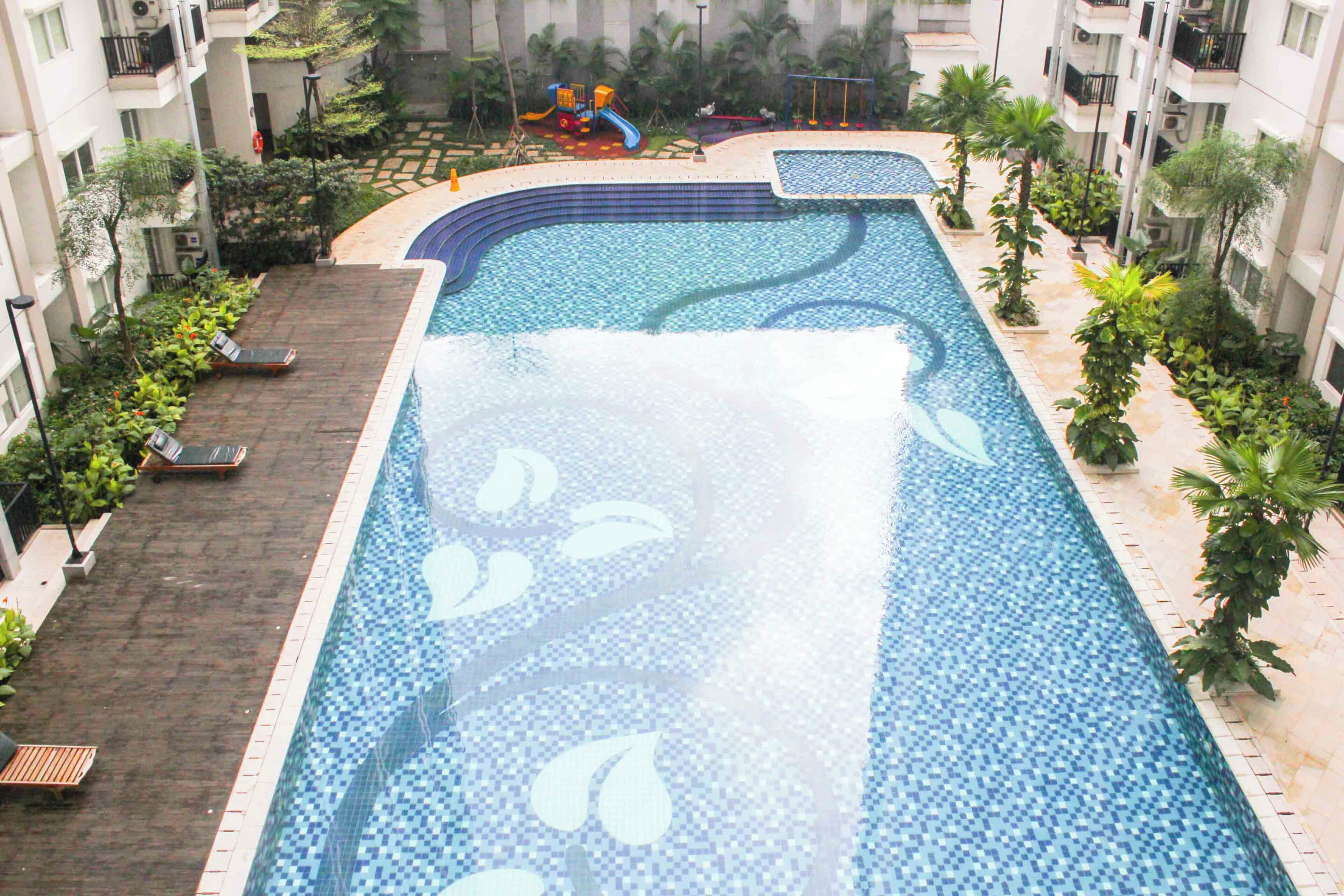 Ein Pool mit Rutsche, umgeben von Grünpflanzen und einer gefliesten Terrasse.