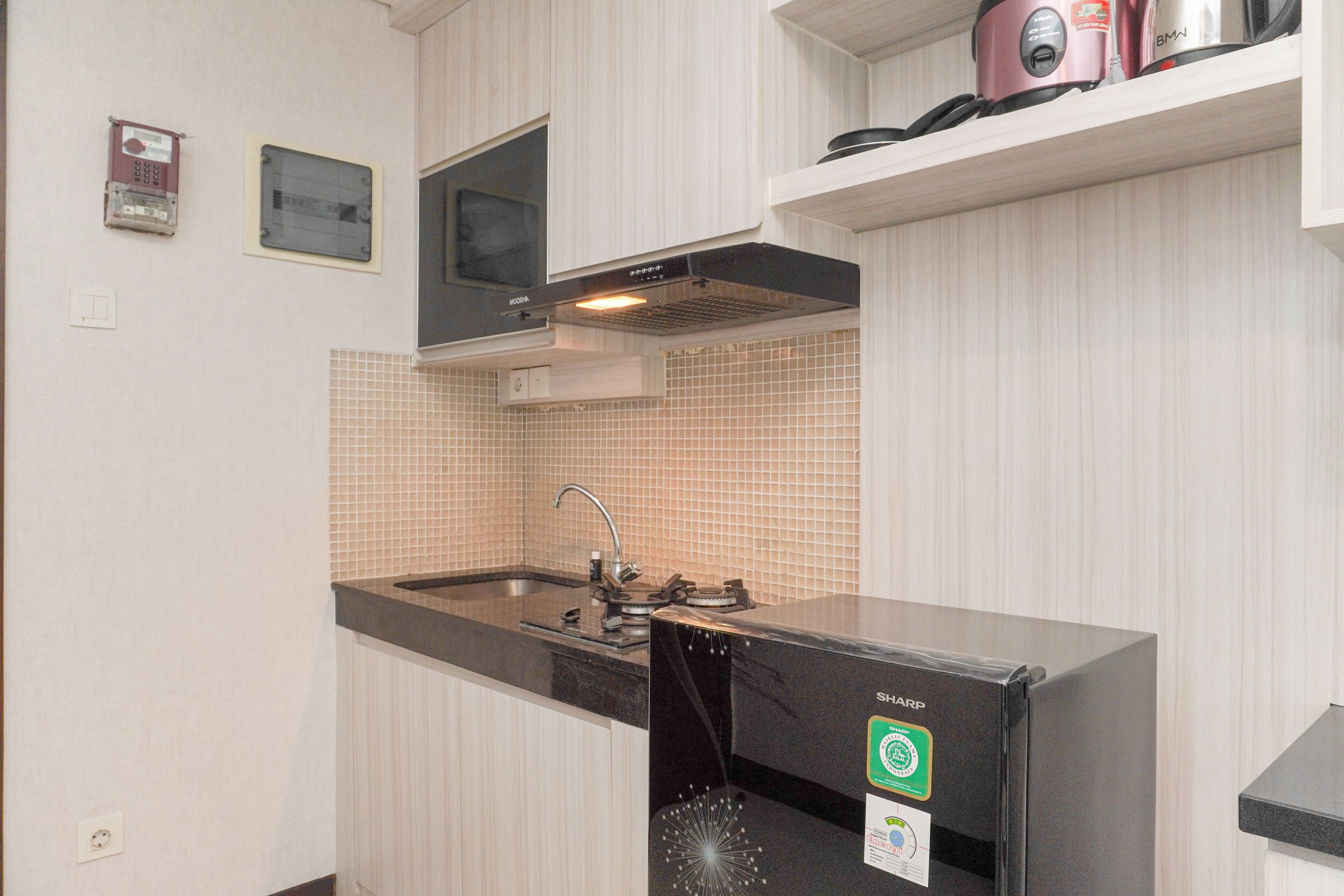 A kitchen with a sink, stove, and microwave. There is a window above the stove and a shelf with kitchen appliances.