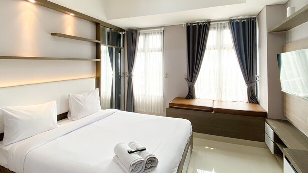 Een moderne hotelkamer met een groot bed, nachtkastje, televisie en raam met gordijnen.