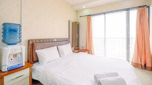 A hotel room with a bed, a water dispenser, a nightstand, a mirror, and a window with curtains. - Cozy Stay Studio At Cervino Village Casablanca Apartment (Jakarta)