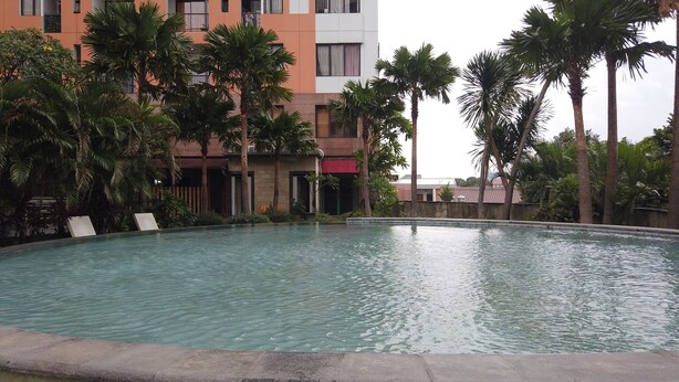 A swimming pool surrounded by palm trees and a multi-story building with balconies. - Cozy Stay Studio At Cervino Village Casablanca Apartment (Jakarta)