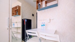A small kitchenette with a refrigerator, a microwave, and a water dispenser. There is a table with two chairs and a shelf above it. - Cozy Stay Studio At Cervino Village Casablanca Apartment (Jakarta)