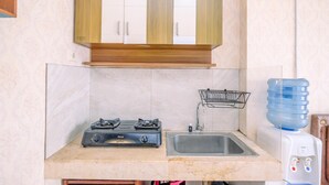 A kitchen with a gas stove, a sink, a water dispenser, and wooden cabinets. - Cozy Stay Studio At Cervino Village Casablanca Apartment (Jakarta)
