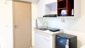 A compact kitchen with a built-in dishwasher, a small refrigerator, and a microwave. - Homey And Simply Look Studio Meikarta Apartment (Cikarang)
