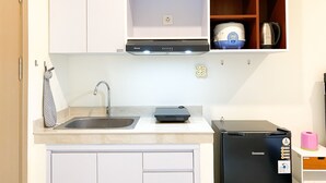 A compact kitchen with white cabinets, a stainless steel sink, a black refrigerator, and a built-in oven. - Homey And Simply Look Studio Meikarta Apartment (Cikarang)