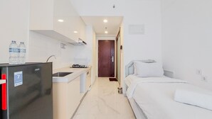 A compact hotel room with a kitchenette, a bed, and a bathroom. - Good Deal And Comfortable Studio At Sky House Bsd Apartment (Pagedangan)