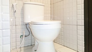 Des toilettes blanches, avec un réservoir et un accessoire de type bidet, dans une salle de bain dont les murs et le sol sont recouverts de carreaux.