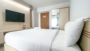 A hotel room with a bed, a TV mounted on the wall, a door, and a mirror. - Cozy Living And Homey Studio Room Cinere Resort Apartment (Depok)