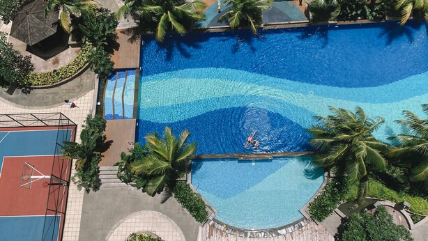 A large, clear swimming pool surrounded by palm trees and a basketball court. - Cozy Living And Homey Studio Room Cinere Resort Apartment (Depok)