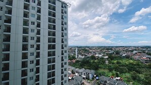 A high-rise building with multiple balconies and a view of a residential area with houses and greenery. - Cozy Living And Homey Studio Room Cinere Resort Apartment (Depok)