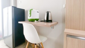 A small kitchenette with a white chair, a green and white coffee maker, and a black electric kettle on a wooden shelf. - Cozy Living And Homey Studio Room Cinere Resort Apartment (Depok)