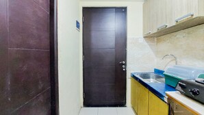 A narrow kitchen with a black door, a sink, and a stove. - Cozy And Minimalist Studio Great Western Apartment (Tangerang)