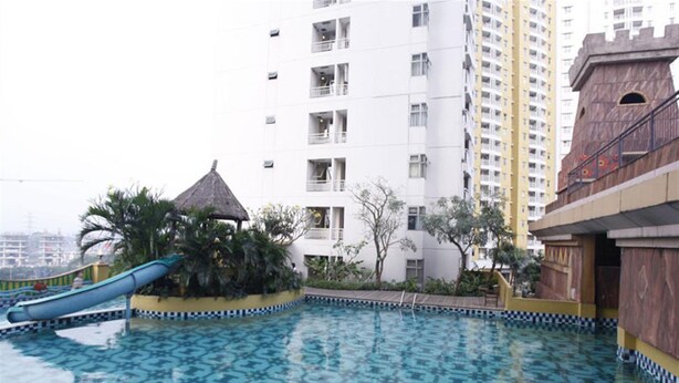 A swimming pool with a slide, surrounded by palm trees and a thatched-roof structure. - Cozy And Minimalist Studio Great Western Apartment (Tangerang)
