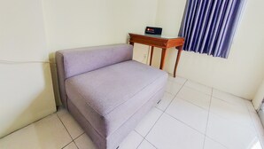 A room with a purple sofa, a small wooden table with a sign, and a window with blue curtains. - Cozy And Minimalist Studio Great Western Apartment (Tangerang)